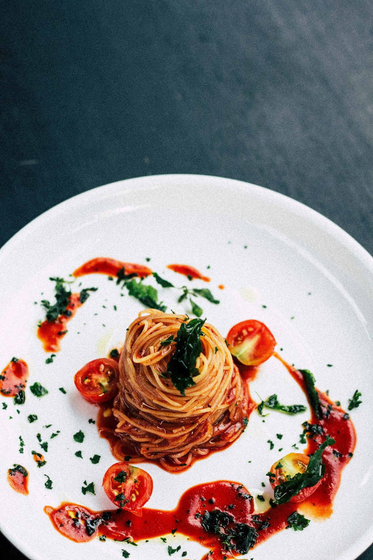 A tower of spaghetti al pomodoro plated on a white dish against dark slate